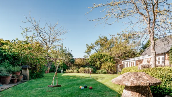 The long croquet lawn of Well Cottage stretching back to the stone wall, with the garden room and flower borders on either side