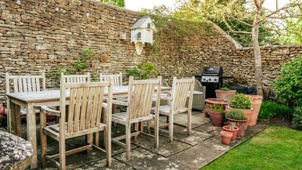 The garden dining table at Well Cottage in late afternoon light, set for a long summer lunch against the stone wall