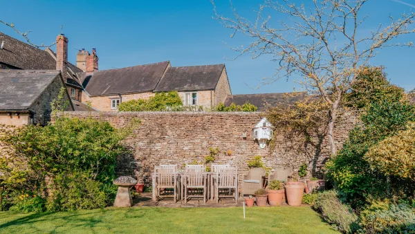 A wide view of the walled garden at Well Cottage in summer, with the croquet lawn, flower beds and dry-stone boundary wall