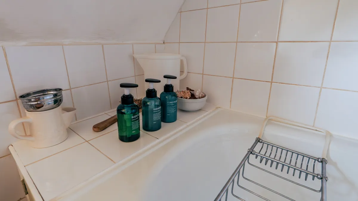 A corner of the upstairs bath — shampoo, conditioner and body wash lined up on the white-tiled edge beneath the sloping eaves