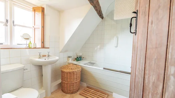 The upstairs bathroom at Well Cottage, white-tiled with a deep bath and eaves ceiling