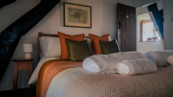 The king bedroom at Well Cottage in daylight, with painted shutters, beamed ceiling and a chest at the foot of the bed