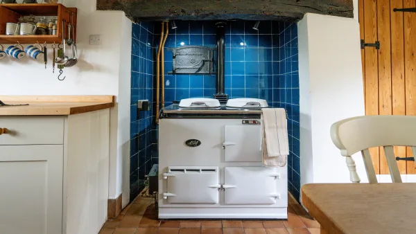 The cream four-oven Aga in the kitchen of Well Cottage, warm in the morning light with the stone wall behind