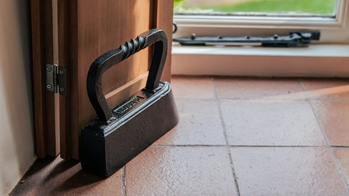 An old cast-iron flat-iron used as a doorstop on the terracotta-tiled floor, holding the timber garden door open to the green beyond