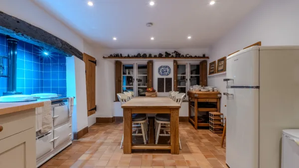 The kitchen at Well Cottage in the evening: warm lamplight on the cream cabinetry, the Aga glowing, the table cleared after supper