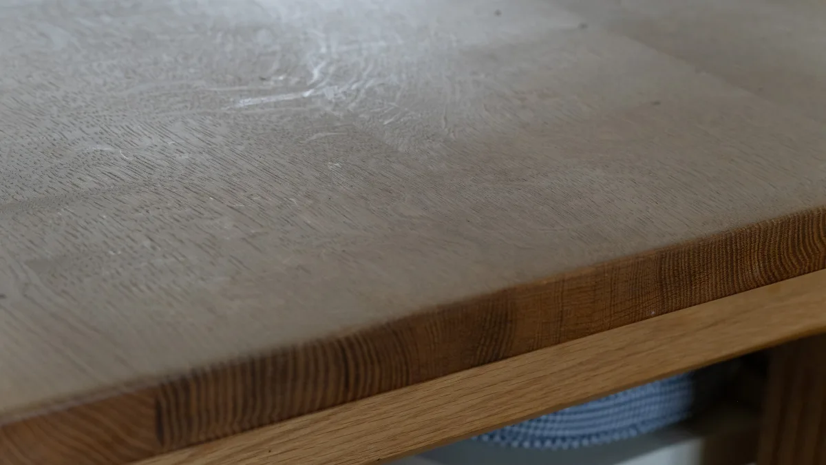A close-up of the chamfered corner of the solid American-oak table top, the pale bleached surface meeting the warmer grain of the edge