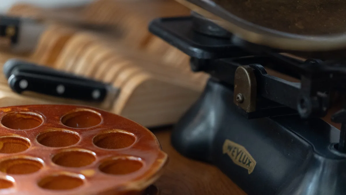 A set of antique black Weylux balance scales on the worktop beside a glazed terracotta bun mould and a kitchen knife on a wooden board