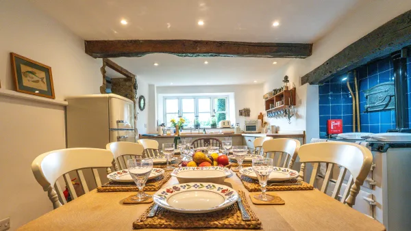 The oak farmhouse table at Well Cottage set for dinner, wine glasses and candles, the Aga warm in the background