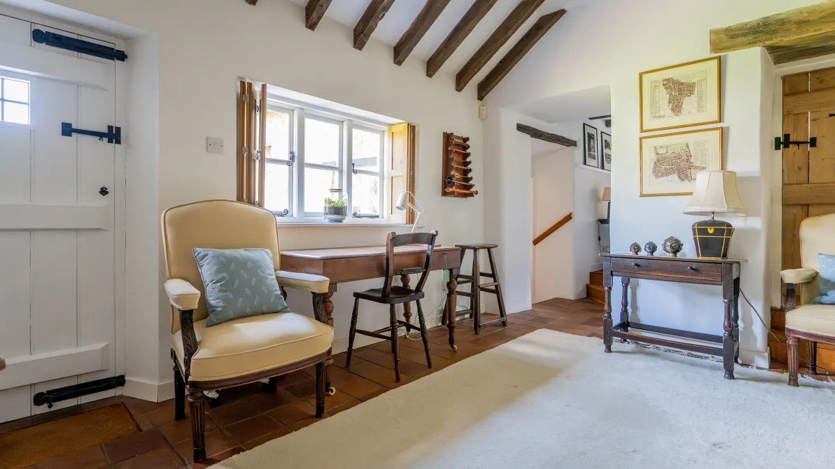 The cream upholstered armchair with a blue cushion beside the writing desk, framed estate maps of Ledwell on the wall behind