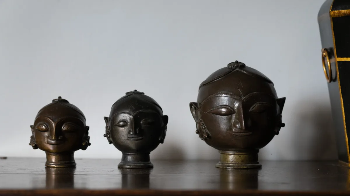 Three antique Indian bronze heads in graded sizes displayed on a dark wooden chest in the library