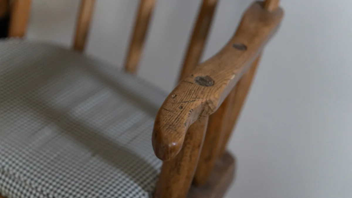 A close detail of the worn, honey-coloured arm of an old country pine chair with its checked cushion seat