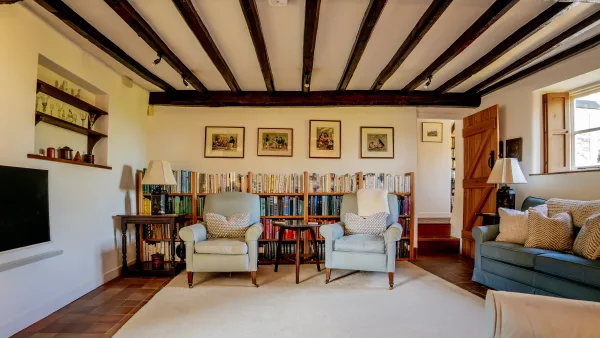 Two pale blue armchairs facing one another in the living room, below a low-beamed ceiling and framed Cotswold prints