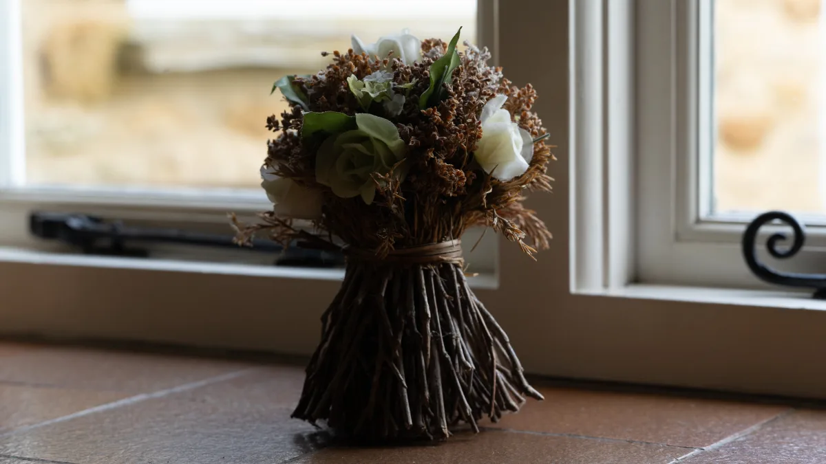 A small dried-twig posy topped with white and green roses, standing on the tiled windowsill