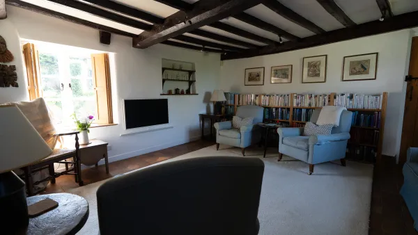 A deep cottage window in the living room looking out to the lane, with a reading chair set beside it in the afternoon light