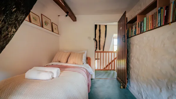 The single bedroom tucked under a great curved timber, with a bookshelf built into the stone wall and a small cottage window