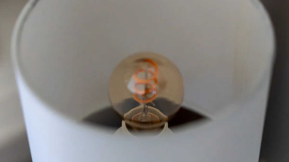 A close view inside a bedside lampshade, the warm spiral filament of the bulb glowing amber