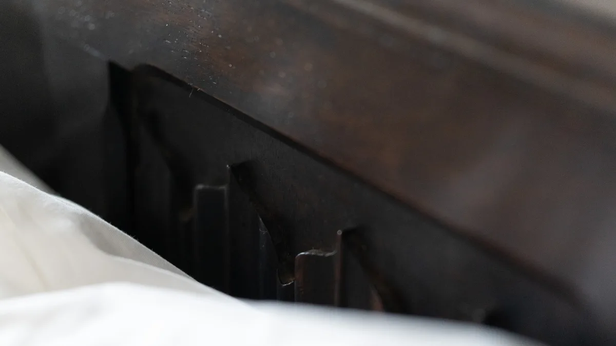 Close detail of the carved linenfold panel on the dark-wood bedstead rising above soft white bedlinen