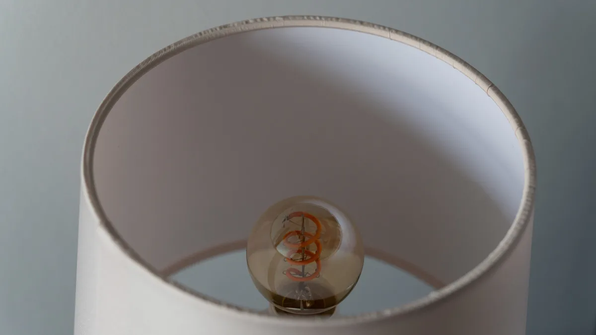 A bedside lamp seen from above, the amber spiral filament bulb sitting within its pale linen shade