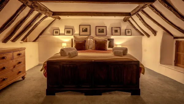 The super-king bedroom at Well Cottage by lamplight, eaves curving overhead and the bed dressed for sleep