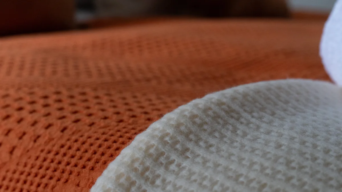 Close detail of a textured burnt-orange waffle blanket meeting a cream waffle throw across the bed