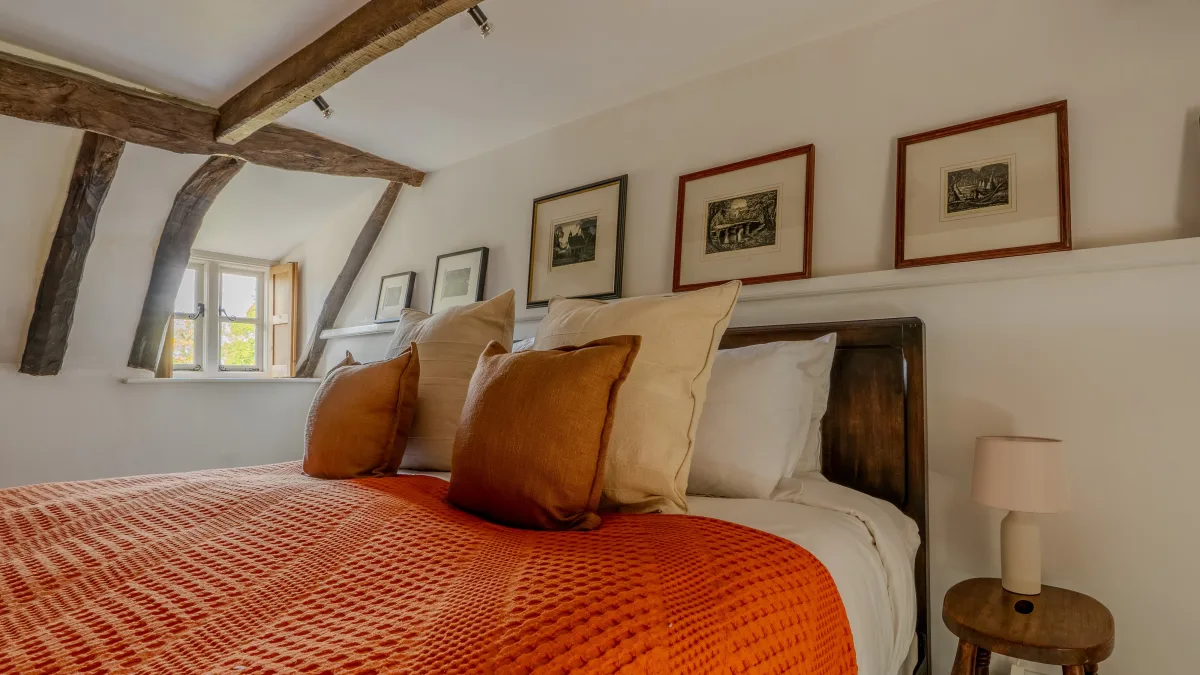 The super king bed dressed in white linen and a burnt-orange waffle blanket, the deep casement window with pine shutter folded open onto the green garden beyond