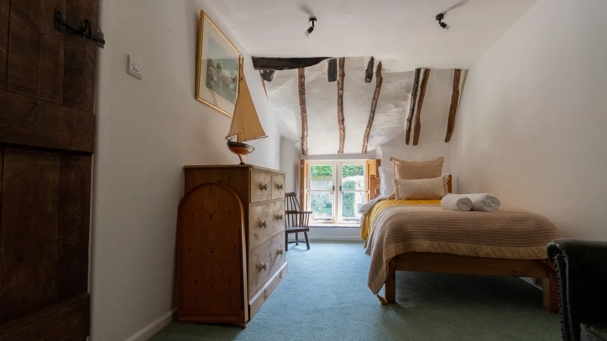 The Twin Room seen from the plank door, the pine dresser and framed painting on the left, a single bed under the beamed eaves with the shuttered window beyond