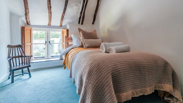 The twin bedroom at Well Cottage under whitewashed beams, with a shuttered window and two single beds on a stripped pine floor