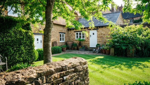 The honey-stone, thatched front of Well Cottage with its namesake stone well beside the garden gate on the village lane