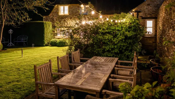 The garden at Well Cottage in the evening, with a long table lit by festoon lights